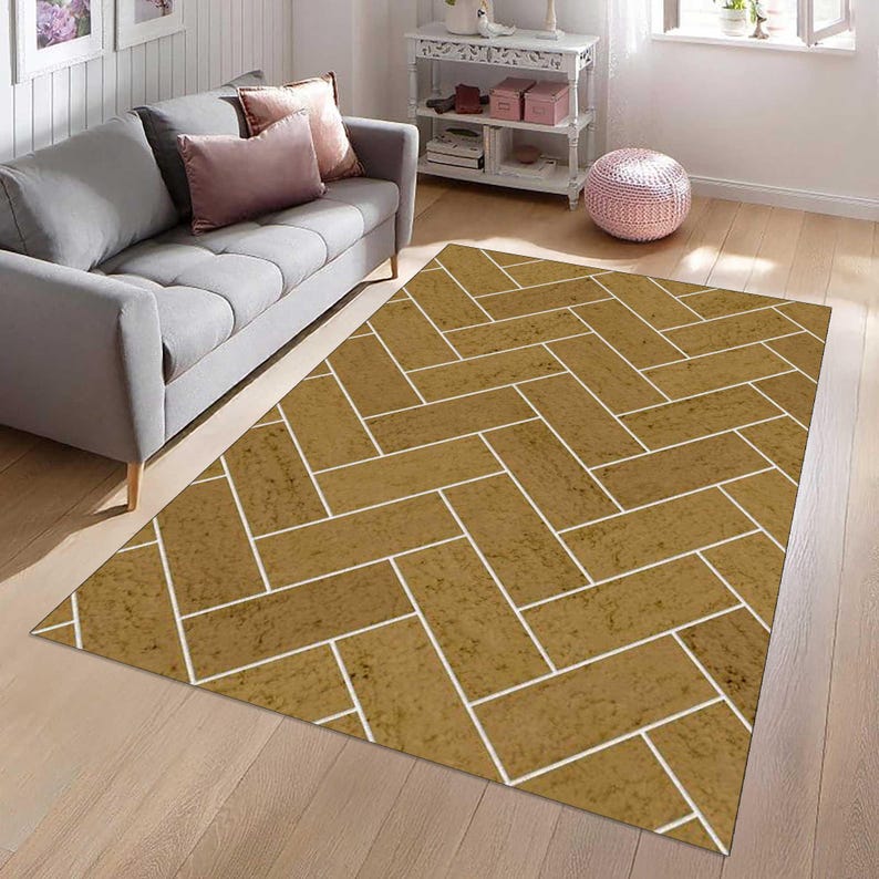 May include: A rectangular area rug featuring a repeating herringbone pattern in a textured golden-brown hue with thin white lines separating each rectangular block. The design covers the entire surface of the rug, creating a geometric layout.