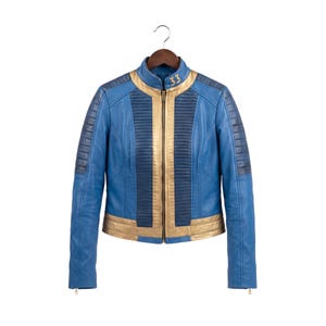 May include: A blue and gold jacket featuring a stand-up collar with the number 33 printed in gold. The jacket has a central gold zipper, vertical pleated panels on the chest, and dark blue ribbed detailing on the shoulders and sleeves.