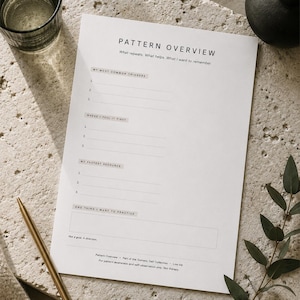 May include: A white Pattern Overview worksheet with prompts for self-reflection, a gold pen, a glass of water, and a small black vase are arranged on a textured surface. The worksheet includes prompts such as "My Most Common Triggers" and "One Thing I Want to Practice."
