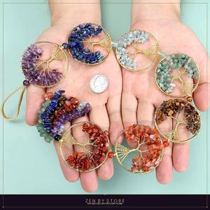 May include: A collection of gemstone tree of life ornaments in various colors, including purple, blue, green, and red. Each ornament features a gold-colored wire tree design within a circular frame. A US quarter is also visible.