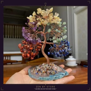May include: A decorative wire tree sculpture featuring clusters of tumbled gemstones in yellow, green, purple, red, and blue. The tree is anchored to a flat, circular blue stone base covered in small, multi-coloured crystal chips.