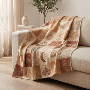 May include: A rectangular throw blanket featuring a grid pattern of squares in shades of cream, tan, and terracotta. Each square displays line art illustrations of butterflies, moths, crescent moons, suns, and various botanical floral elements.