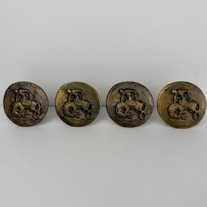 May include: A set of four circular bronze-toned metal buttons, each featuring a raised relief design of a centaur figure. The buttons have a weathered, metallic finish with dark patina accents highlighting the detailed mythological creature.
