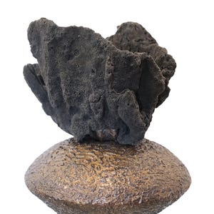 Può includere: Unica scultura artigianale con una forma scura e porosa simile a una roccia sopra una base strutturata color bronzo. Il design astratto e organico è adatto all'arredamento della casa.