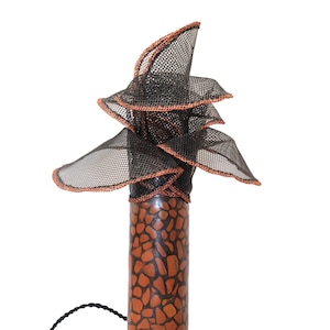 Può includere: Lampada da tavolo decorativa con base cilindrica con un motivo a pietre marroni e nere. La parte superiore della lampada ha un design a strati, a forma di fiore, realizzato in rete nera con finiture color rame. Un cavo nero si estende dalla base.