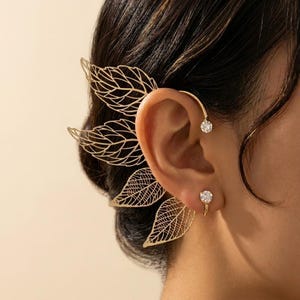 Peut inclure: Ensemble de boucles d'oreilles et de manchette d'oreille dorées. La manchette d'oreille présente un motif de feuilles délicat, tandis que la boucle d'oreille et la manchette sont ornées de pierres précieuses rondes et transparentes.