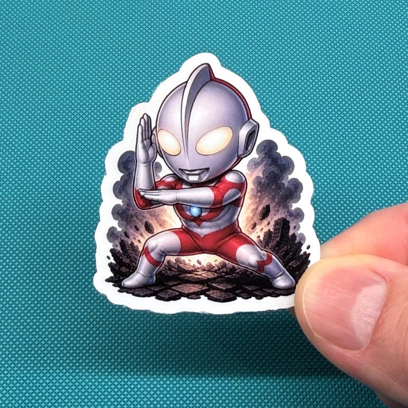 Op de afbeelding: Een sticker met een chibi-stijl karakter in een rood en wit pak, in een vechtkunsthouding. Het karakter heeft een zilveren helm en gloeiende gele ogen. De achtergrond toont een rokerige, rotsachtige sc&egrave;ne.