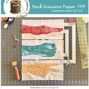 May include: Three rectangular fabric quilt blocks featuring Rock Scissors Paper FPP patterns, each measuring 12.5 inches by 6 inches. The blocks display abstract shapes in red, teal, and yellow floral prints, arranged on a dark gray cutting mat.