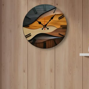 May include: A round wooden wall clock with a layered design. The clock face features a wave-like pattern in shades of black, brown, and tan. Black hands and hour markers contrast against the lighter wood tones. The clock is mounted on a wooden wall.