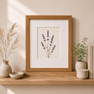 May include: A framed print of a lavender sprig illustration in purple and green hues. The artwork is set against a cream background, within a wooden frame. The image is displayed on a wooden shelf with decorative vases and books.