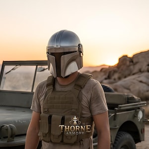 May include: A silver-colored helmet with a T-shaped visor and a tan tactical vest featuring multiple pouches. The vest displays the text THORNE ARMORY with a crown logo. The helmet has a smooth, metallic finish and a dark, recessed faceplate.