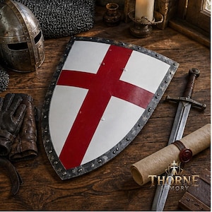 Puede incluir: Un escudo heráldico con superficie blanca y una cruz roja, bordeado por un marco de metal oscuro con remaches visibles. El escudo se muestra junto a un casco de metal, guantes de cuero, una espada larga y un pergamino con el texto THORNE ARMORY.