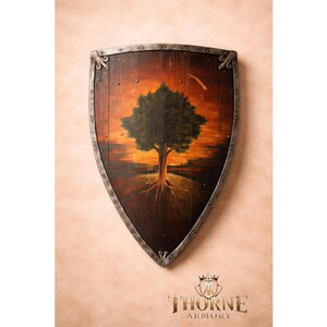 Op de afbeelding: Een houten schild met een donkerbruine afwerking en een metalen rand met decoratieve klinknagels. Het midden toont een geschilderde boom tegen een zonsondergang met oranje en rode tinten. De tekst Thorne Armory staat onderaan afgebeeld.
