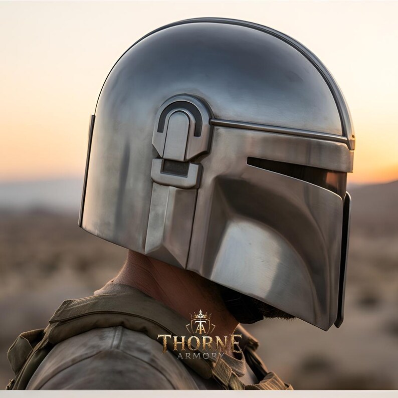 May include: A polished silver-toned metal helmet with a smooth, rounded dome and a T-shaped visor opening. The side features a rectangular ear piece detail. The text Thorne Armory is visible at the bottom center of the image in gold lettering.