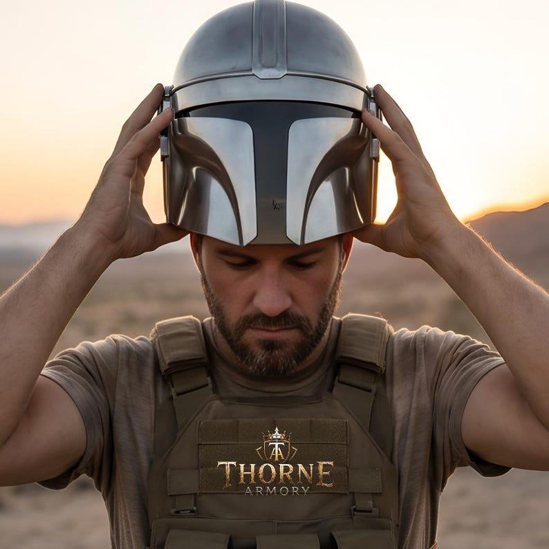 May include: A metallic silver helmet with a dark visor and a central T-shaped faceplate. The helmet is worn over a tan tactical vest featuring a patch with a crown logo and the text THORNE ARMORY in gold lettering against a desert background.