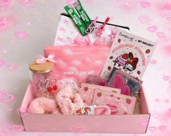 May include: A pink gift box containing beauty items. It features a jar with a wooden lid, a pink scrunchie, lip masks, eye masks, and a box labelled "PDRN GLOW KIT". The box also includes a "Strawberry Sweetness" face mask and matcha sachets.
