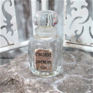 Puede incluir: Un frasco de perfume de vidrio transparente con una etiqueta dorada que dice "L'Interdit Givenchy Paris France".