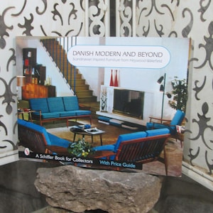 Puede incluir: Una portada de libro con una foto de una sala de estar con una chimenea, un sofá y sillas. El título del libro es "Danish Modern and Beyond: Scandinavian Inspired Furniture from Heywood-Wakefield". El libro es un Schiffer Book for Collectors con una guía de precios.