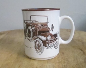 Könnte beinhalten: Weißer Keramikbecher mit braunem Rand und Henkel, verziert mit einer braunen Oldtimer-Illustration. Das Auto-Design umfasst Räder, Scheinwerfer und eine Windschutzscheibe. Der Becher ist für Getränke geeignet.