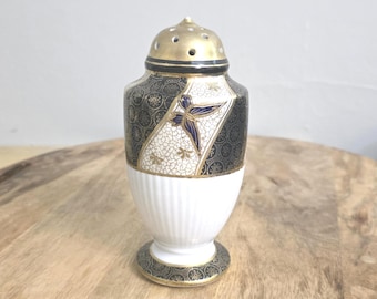 Könnte beinhalten: Ein Keramikstreuer mit einem goldfarbenen, perforierten Deckel, einem weißen, geriffelten Fuß und einem schwarzen Oberteil, das mit filigranen goldenen Blumenmustern und einem blauen Schmetterlingsmotiv verziert ist. Der Fuß hat einen Rand.