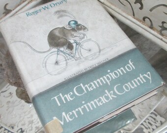 Könnte beinhalten: Ein Vintage-Kinderbuch mit dem Titel "The Champion of Merrimack County" von Roger W. Drury, illustriert von Fritz Wegner. Der Umschlag zeigt eine Schwarzweißillustration einer Maus, die Fahrrad fährt.