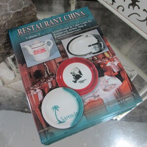 May include: A book titled "RESTAURANT CHINA Volume 2" with images of restaurant china, including a teapot and plates. The book cover features a red and white plate with a graphic and a blue and white plate with the text "SAMBO'S".