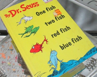 Op de afbeelding: Een geel boek met de titel "By Dr. Seuss One fish two fish red fish blue fish" met illustraties van kleurrijke vissen.
