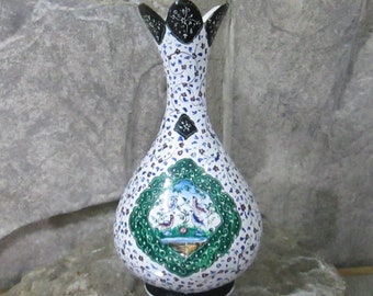 Könnte beinhalten: Eine weiße Keramikvase mit einem grünen, blauen und weißen Blumendesign und einem schwarzen Rand. Die Vase hat einen breiten Boden und einen schmalen Hals.