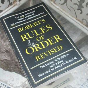 May include: A black book titled "Robert's Rules of Order Revised" with yellow lettering. The book is the classic 1915 edition with a new foreword by Henry M. Robert III.