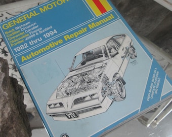 Op de afbeelding: Een Haynes Automotive Repair Manual voor General Motors voertuigen van 1982 tot 1994. De cover is lichtblauw met een auto-illustratie en het Haynes-logo. De handleiding behandelt Buick Skyhawk, Cadillac Cimarron en andere modellen.