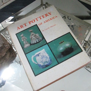 May include: A book titled "Art Pottery of America" by Lucille Henske. The cover features four images of pottery: a pitcher with a blue and white rooster design, a green glazed bowl, and two figurines.