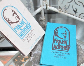 Op de afbeelding: Twee exemplaren van het boek "The Boy Who Made $1,000,000 With A Toy" van Frank Horhby. De boekomslagen zijn blauw en wit met een bruine illustratie van een mannenhoofd.