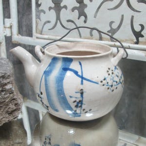 Könnte beinhalten: Eine weiße Teekanne aus Keramik mit einem abstrakten Design in Blau und Schwarz. Die Teekanne hat einen Henkel und einen Ausguss.