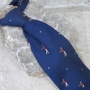 May include: A navy blue silk tie with a repeating pattern of golfers in red, white, and brown. The tie has small yellow dots scattered throughout the pattern.