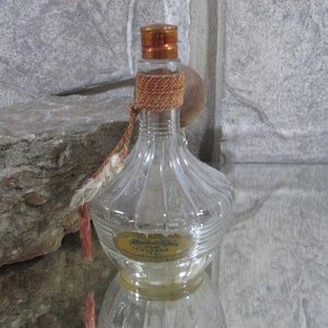 Puede incluir: Una botella de vidrio transparente con un borla roja y dorada y una etiqueta que dice "Marcella's Cologne".