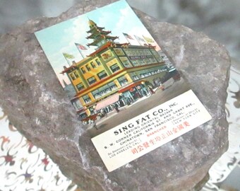 Könnte beinhalten: Eine alte Postkarte mit einem mehrstöckigen Gebäude mit einem Pagodendach. Das Gebäude ist mit "Sing Fat Co., Inc." beschriftet und als "Führender Orientalischer Basar" in Chinatown, San Francisco, Kalifornien, beschrieben. Die Postkarte listet auch Filialen in Los Angeles, Kalifornien und New York City auf.
