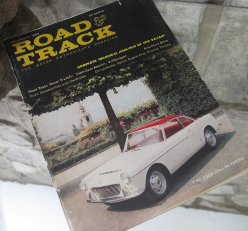 May include: A vintage magazine cover featuring a white Fiat-O.S.C.A. 1500 by Farina car with a red roof. The magazine is titled "Road & Track" and the cover text includes "The Motor Enthusiasts' Magazine" and "Complete Technical Analysis of the Valiant".