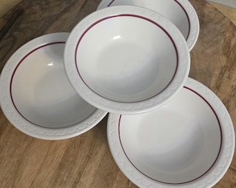 Op de afbeelding: Een set van drie witte keramische kommen met een dieprode cirkelvormige band rond de binnenrand en een subtiel reliëfpatroon langs de buitenrand. De kommen zijn in een groep gerangschikt en tonen hun gladde, glanzende afwerking.