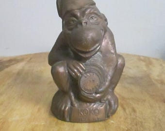 Op de afbeelding: Bronskleurig apenbeeldje, met een fez en een munt. De munt leest "Save for Koko". De basis van het beeldje is gegraveerd met "Koko The Wise".