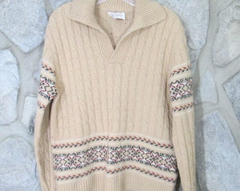 Könnte beinhalten: Ein beiger Kabelstrickpullover mit V-Ausschnitt und einem bunten geometrischen Muster an den Ärmeln und am Saum.