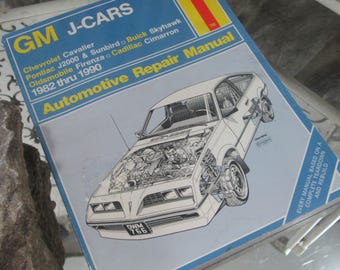 Op de afbeelding: Een Haynes Automotive Repair Manual voor GM J-Cars, inclusief Chevrolet Cavalier, Pontiac J2000 & Sunbird, Buick Skyhawk, Oldsmobile Firenza en Cadillac Cimarron modellen van 1982 tot 1990. De omslag toont een gedetailleerde auto-illustratie.