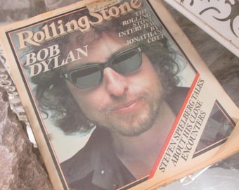 Op de afbeelding: Een vintage Rolling Stone magazine met Bob Dylan op de cover. De titel van het tijdschrift en Dylan's naam zijn prominent aanwezig, samen met tekst over een interview en Steven Spielberg. Het tijdschrift heeft een versleten uitstraling.