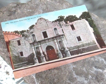 Könnte beinhalten: Eine Vintage-Postkarte, die das Alamo zeigt, eine historische Mission in San Antonio, Texas. Die Postkarte zeigt ein Foto der Fassade des Gebäudes mit seinen weiß getünchten Wänden, gewölbten Türen und kleinen Fenstern. Der Text auf der Postkarte lautet "7578. The Alamo. Built 1718. San Antonio, Texas."