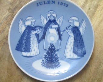 Könnte beinhalten: Blau-weiße Zierteller mit drei Engelsfiguren mit Flügeln, Umhängen und Heiligenscheinen, die einen Weihnachtsbaum umgeben. Auf dem Teller steht in blauer Schrift "JULEN 1972". Der Teller hat einen weißen Rand.
