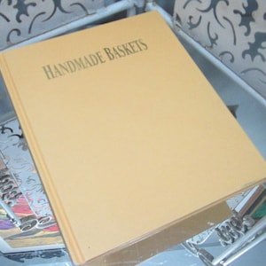 Puede incluir: Un libro amarillo con el título "HANDMADE BASKETS" impreso en letras doradas en la portada.