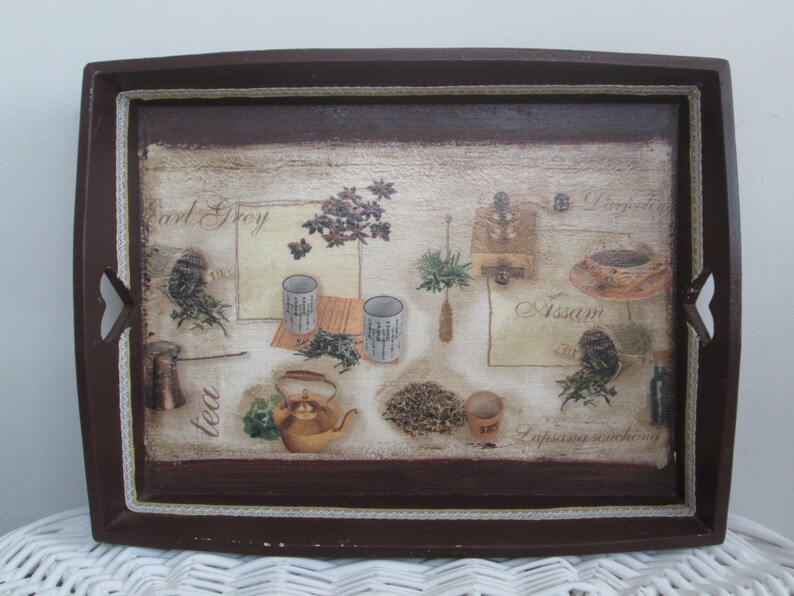 May include: A rectangular brown serving tray with a decorative tea-themed design. The tray features images of tea leaves, teacups, a teapot, and text labels like "Earl Grey" and "Assam". The tray has cut-out handles and a white lace trim.