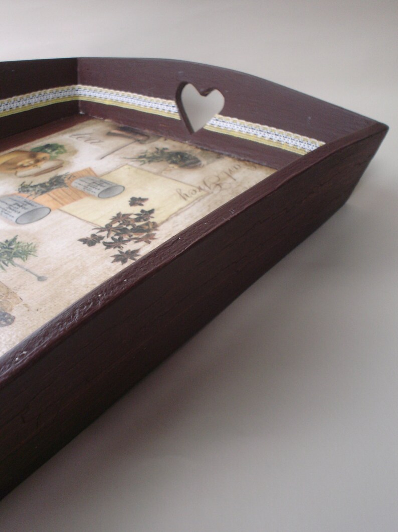 May include: A dark brown wooden serving tray with a heart-shaped cutout on one side. The tray's interior features a vintage-style botanical print with herbs and gardening tools. A decorative white and yellow lace trim borders the print.