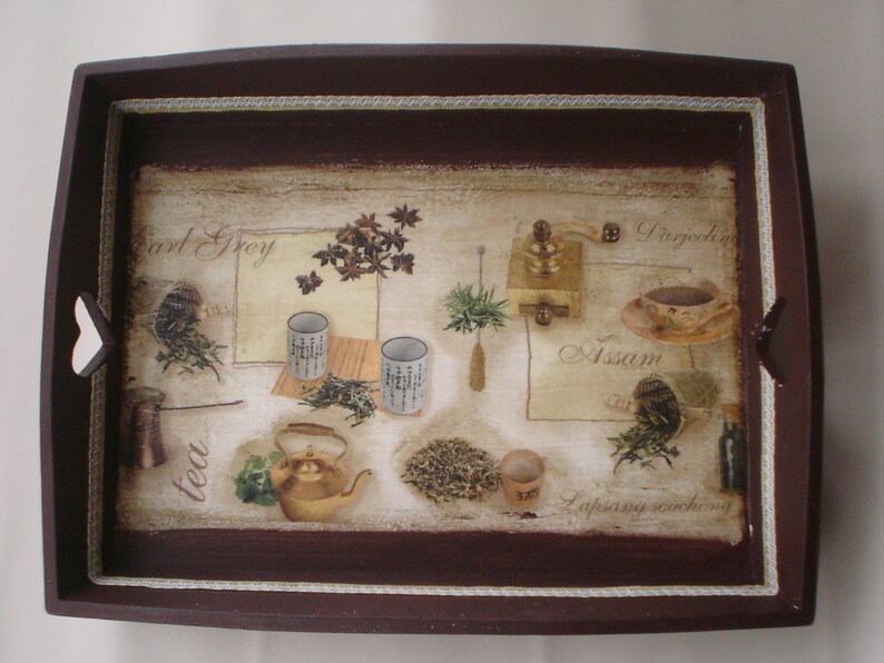 May include: A rectangular wooden serving tray with a dark brown border and heart-shaped cutouts on the sides. The tray's surface features a tea-themed design with illustrations of tea leaves, cups, a teapot, and a grinder. The words "Earl Grey", "Darjeeling", "Assam", and "Lapsang souchong" are also visible.