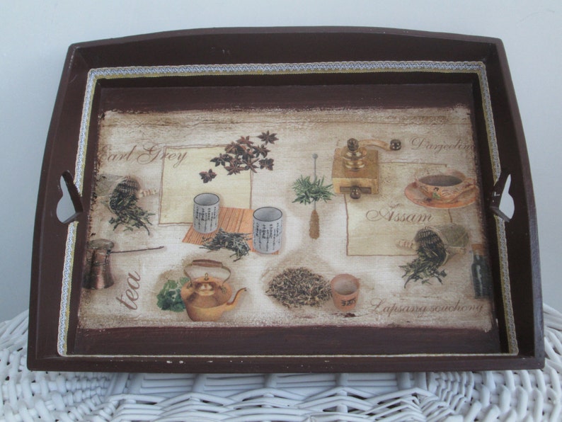 May include: A rectangular brown serving tray with a decorative tea-themed design. The tray features images of tea leaves, teacups, a teapot, and a coffee grinder. The words "Earl Grey", "Assam", and "tea" are visible on the tray.