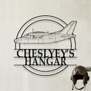 May include: A black metal wall sign featuring a circular frame with a side-profile outline of a twin-engine airplane. Below the airplane, the text reads CHESLYEY'S HANGAR in bold, capitalized letters, integrated into the circular design structure.